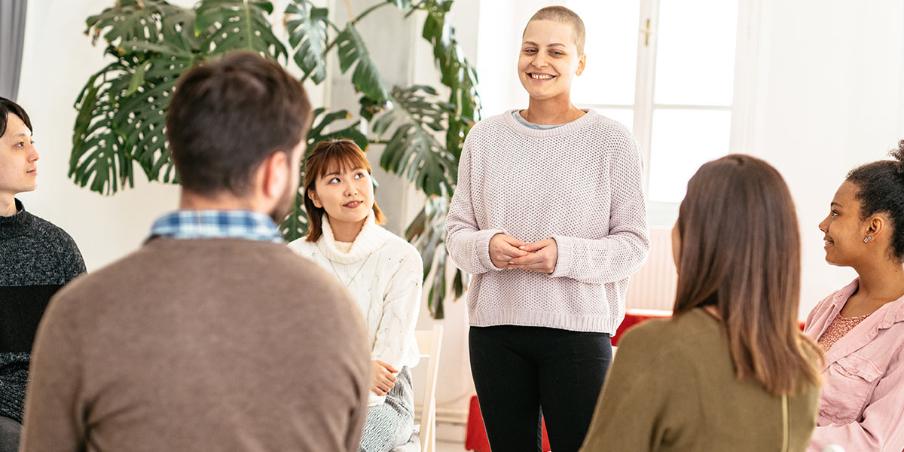 A woman stands smiling in a circle of people on chairs