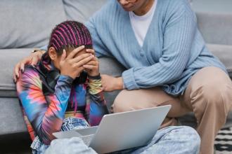 
		Teenager sits desperately in front of a laptop and is touched on the shoulders by an adult
	