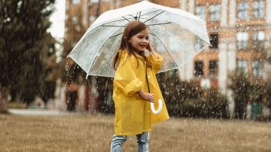 
		Cheerful little girl standing in the rain with an umbrella
	