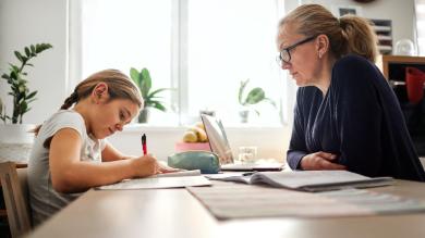 
		Mother sits at the table with child and helps with homework
	