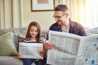 Father sitting on the sofa with his young daughter reading the newspaper together