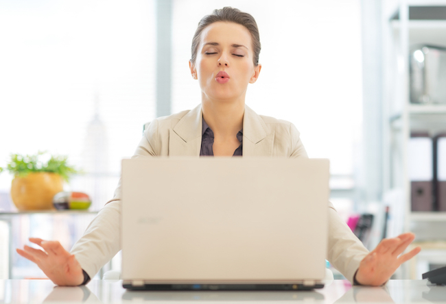Woman sits in front of a laptop, closes her eyes and takes a deep breath.