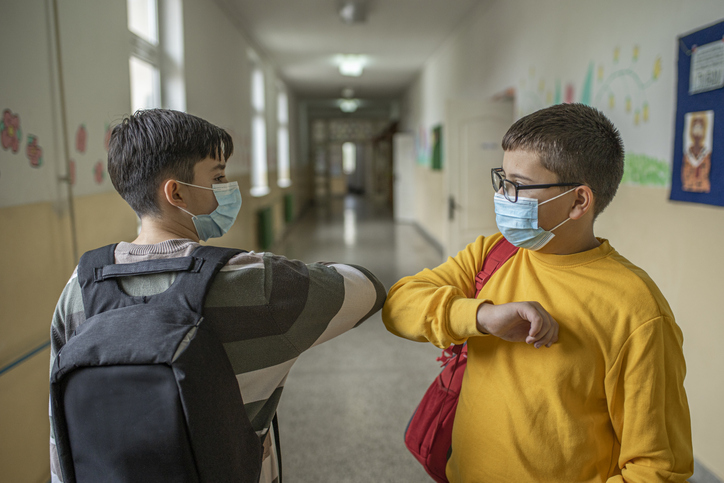 Two schoolchildren greet each other at school with masks and elbows.