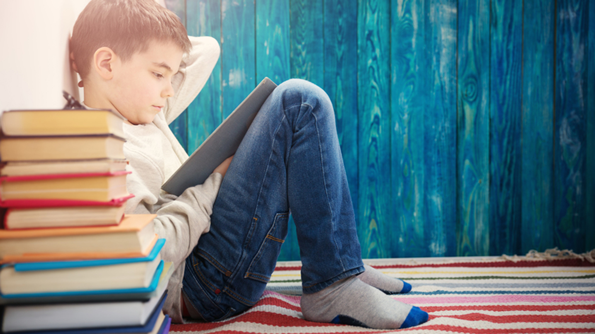 Eight-year-old child reading a book at home. Boy learning on a blue background.