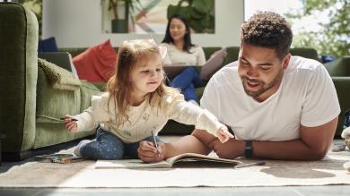 
		Father with his daughter sitting on the living room floor and planning finances
	
