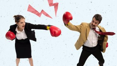 
		A woman and a man in business attire are wearing boxing gloves and want to attack each other
	