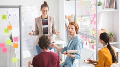 
		Ein Team aus vier Männer und Frauen diskutieren gemeinsam in einem Büro. Sie sitzen vor einer Wand mit Notizen und Zetteln, die sie erarbeitet haben.
	