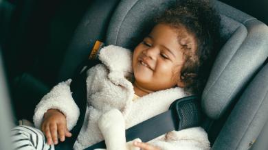 
		Little baby sits in the car seat and laughs
	