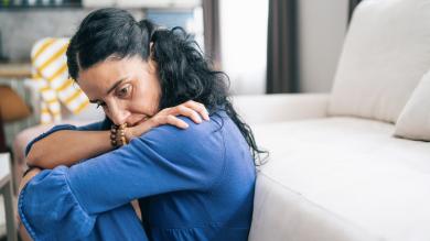 
		A woman sits on the floor at home and looks down anxiously
	