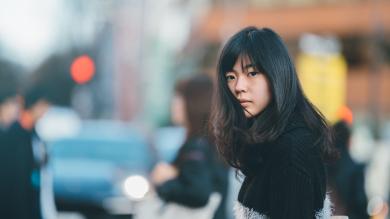 
		A young Asian woman on the street looks anxiously into the camera
	