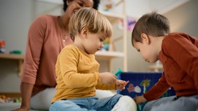 
		Two toddlers play and a caregiver watches
	