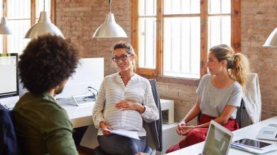 
		Pregnant woman discusses with colleagues in the office and has a hand on her stomach.
	