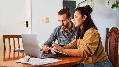 
		A pregnant woman and her husband sit on the sofa with bills and try to get an overview of their finances
	