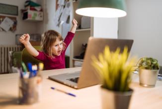 
		A child throws his arms up in the air in front of his laptop
	