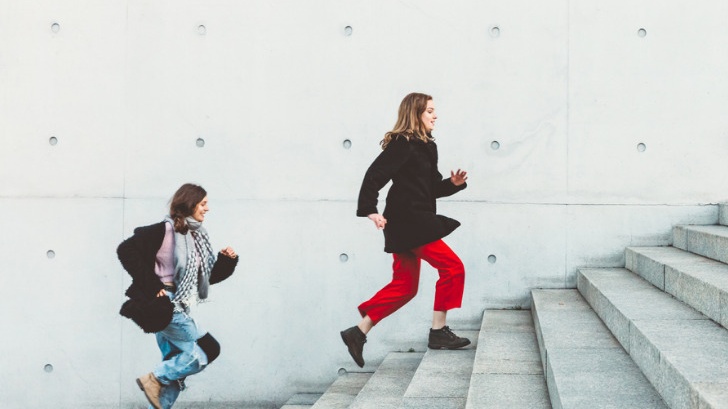 Two women run up the stairs one after the other