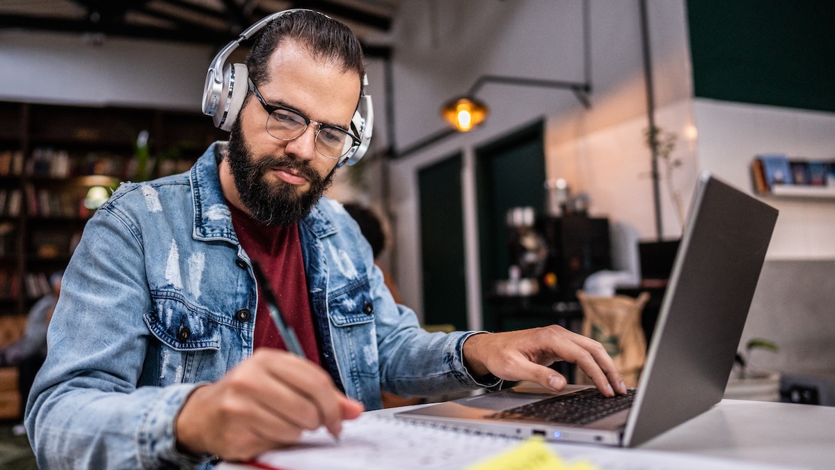 A man wearing headphones is sitting at his laptop