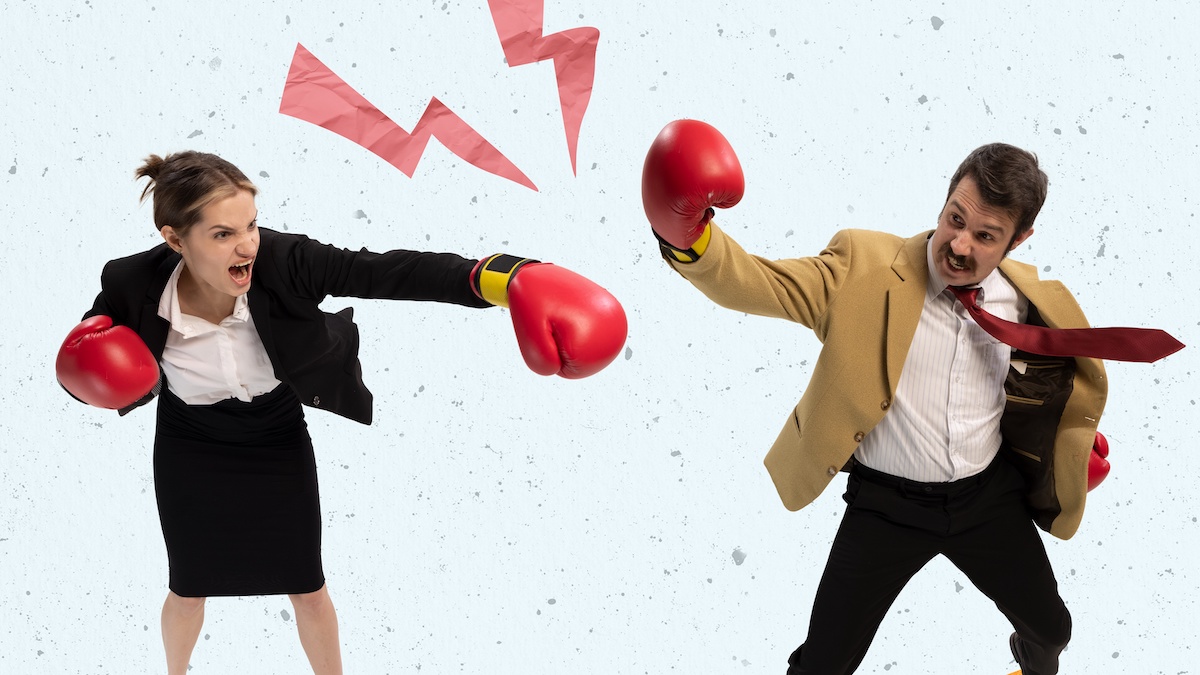 A woman and a man in business attire are wearing boxing gloves and want to attack each other