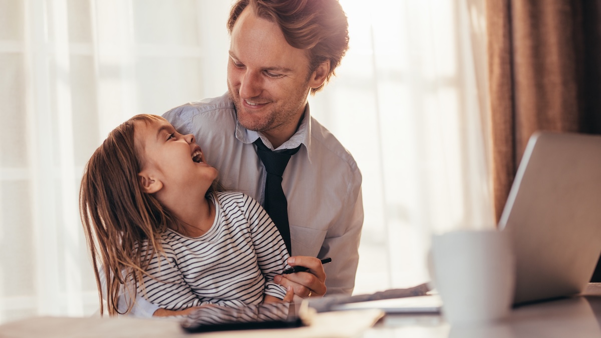 Father sits in front of laptop with child on his lap
