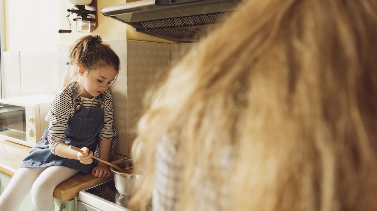A girl is sitting on the kitchen counter and cooking with her mother