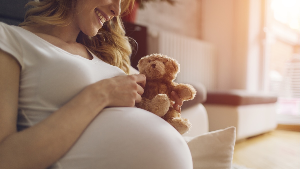 Pregnant woman smiles at her belly and holds a teddy bear