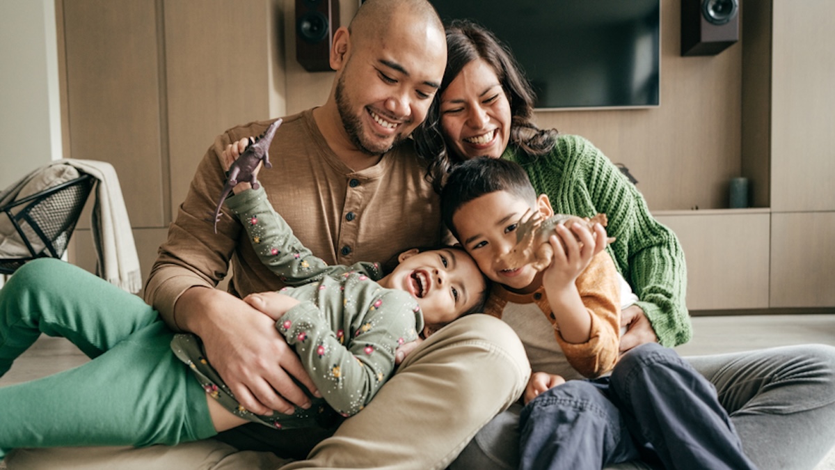 Parents with two children sit laughing together on the floor in the living room