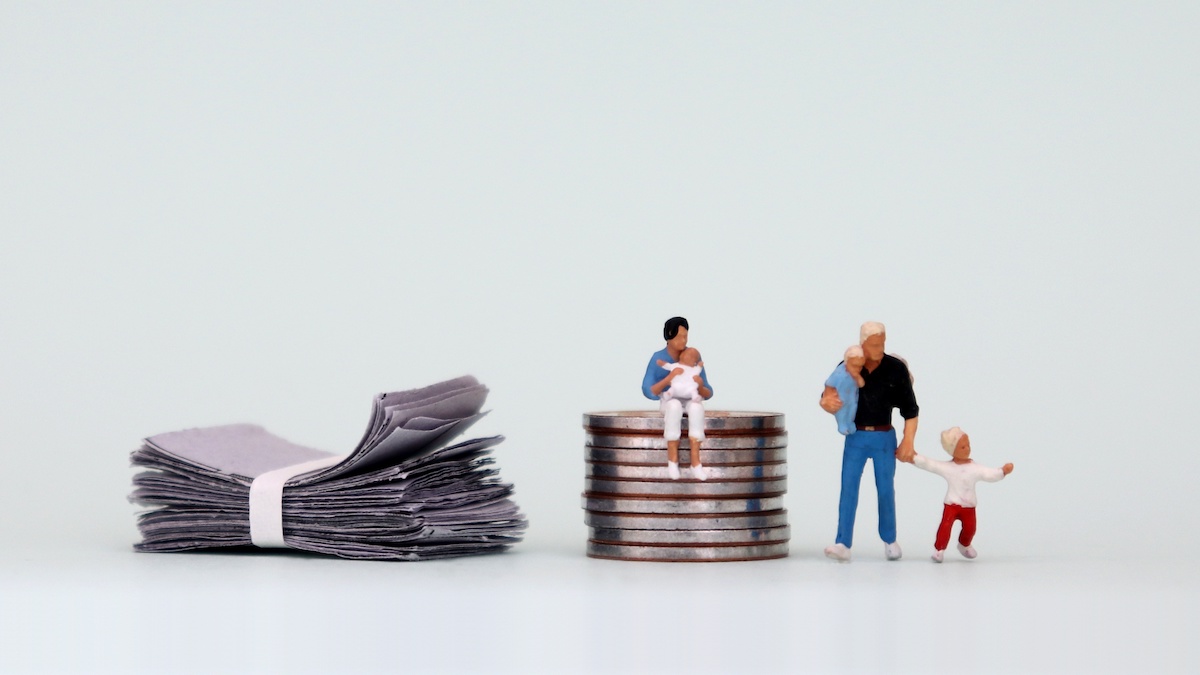 A miniature woman with a baby sits on a pile of coins next to a pile of bills and a miniature man with a baby next to them.