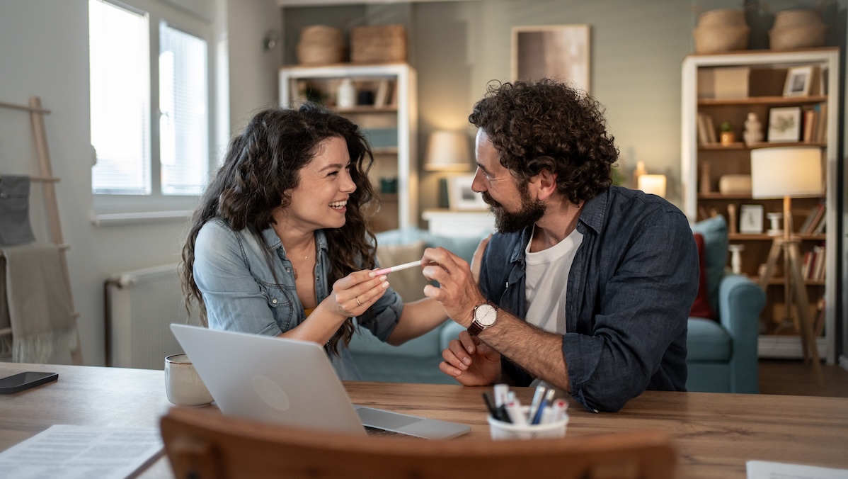 A couple is sitting at the table, delighted by a positive pregnancy test
