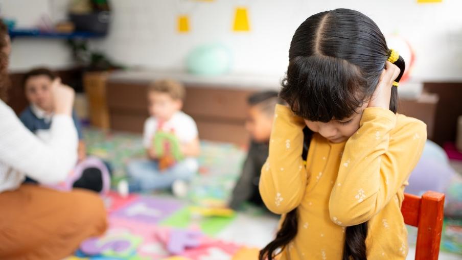 An autistic girl covers her ears at preschool