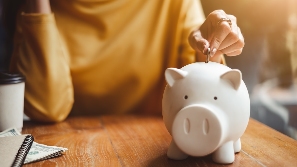 A hand throws a coin into a piggy bank