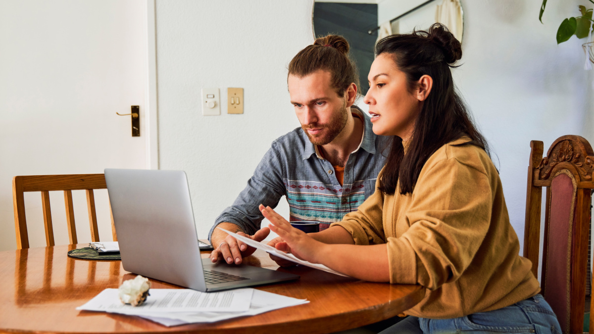 A pregnant woman and her husband sit on the sofa with bills and try to get an overview of their finances