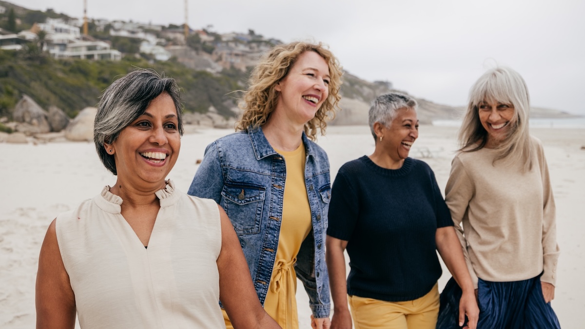 Four menopausal women walk together on the beach and laugh