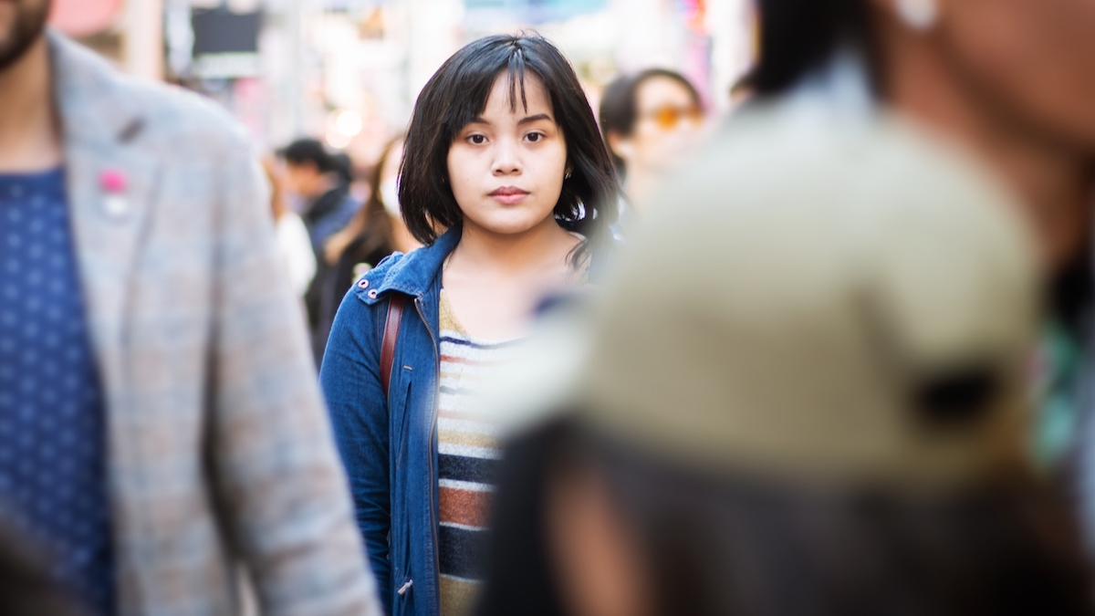 Young girl stands with a sad look in a blurred crowd