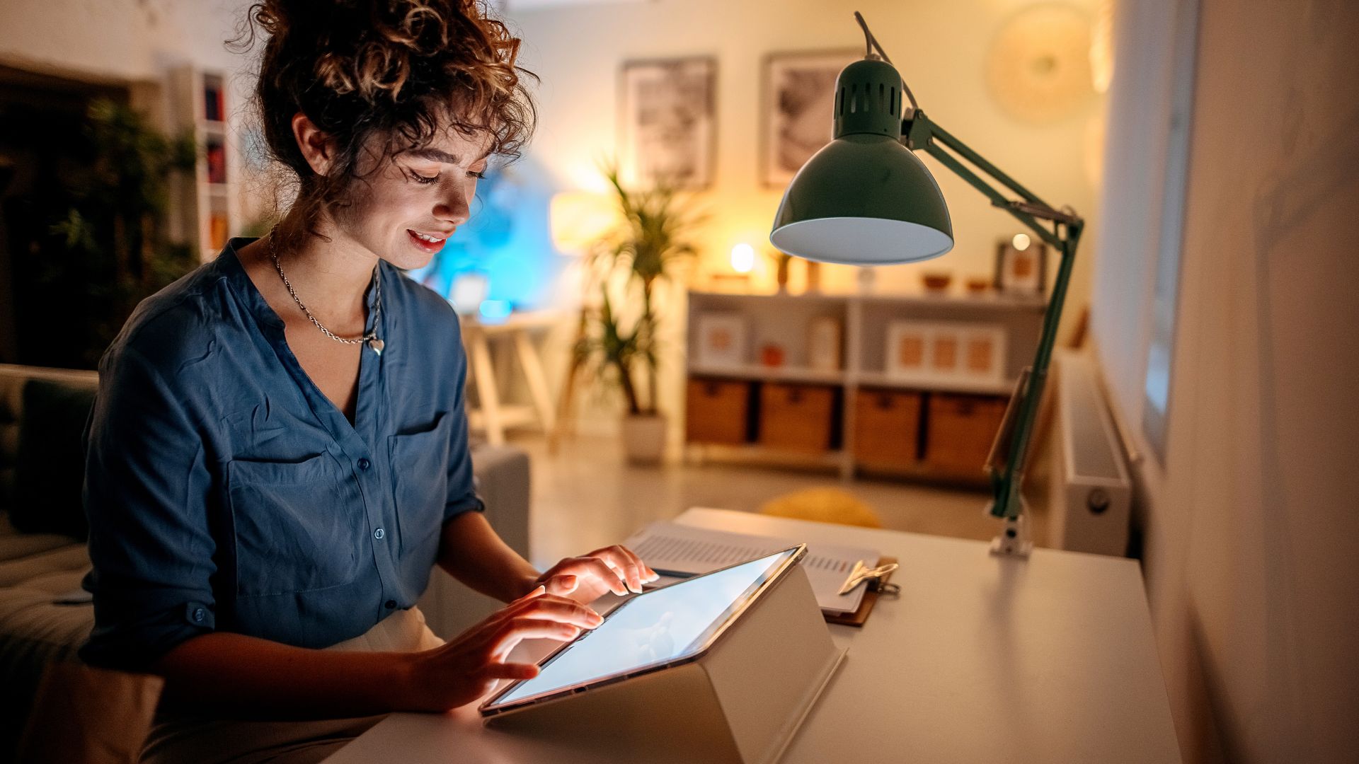 A woman is sitting at her desk at home, using a tablet