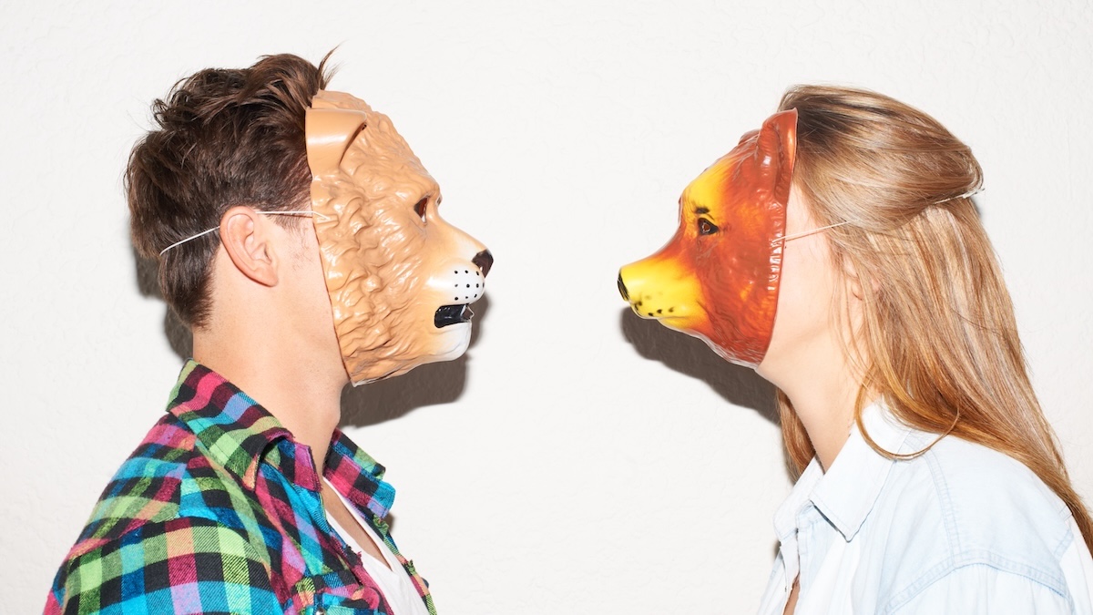 Two people wearing animal masks stand opposite each other and look at each other