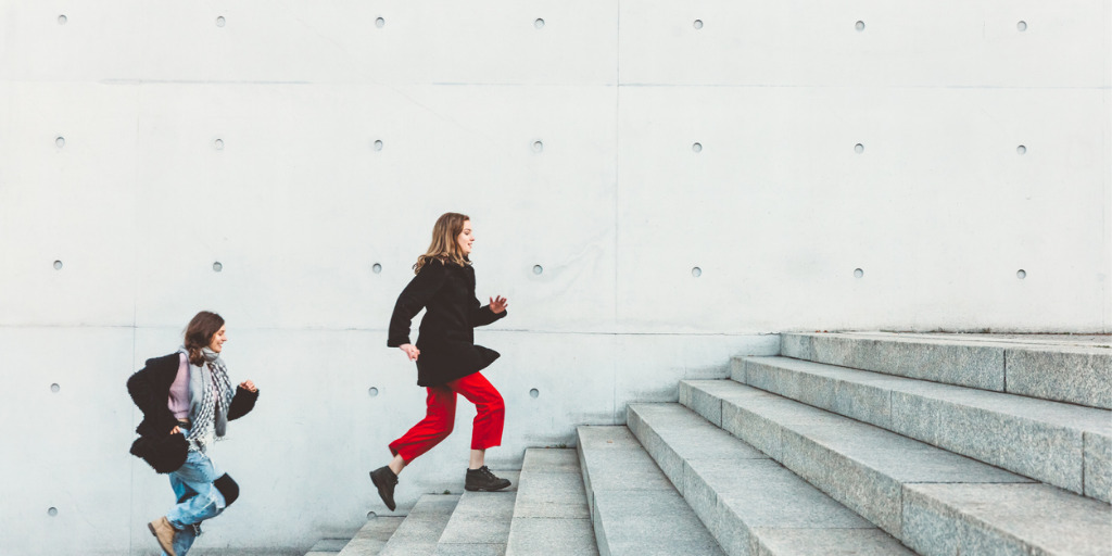 Two women run up the stairs one after the other