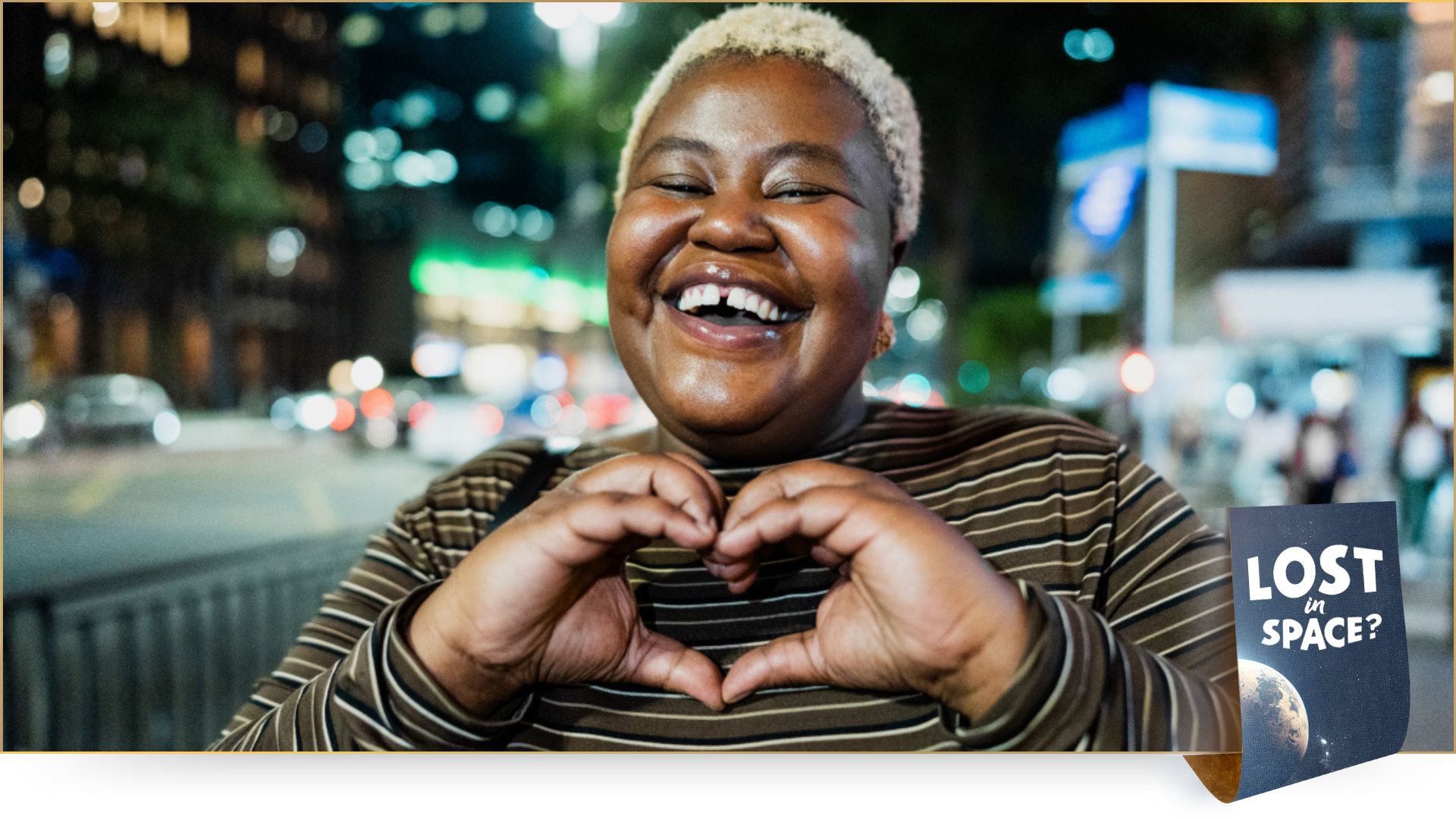 A woman forms a heart with her hands in front of her chest and laughs
