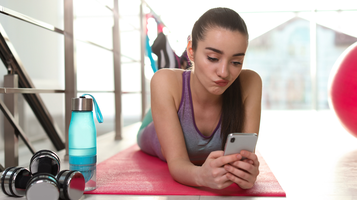 Woman with cell phone lazing on yoga mat