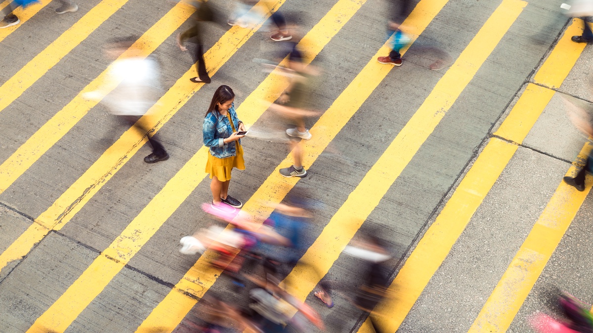 A woman walks across a yellow crosswalk and types something on her smartphone