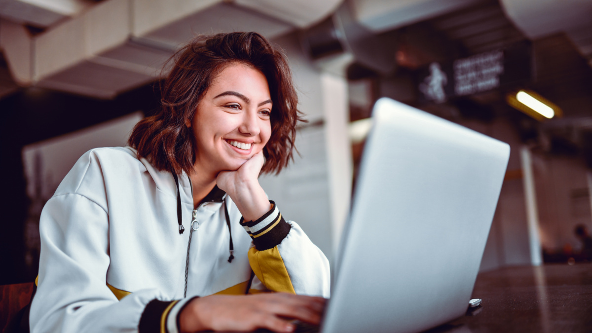 A young woman sits laughing in front of her laptop in the office and changes her password