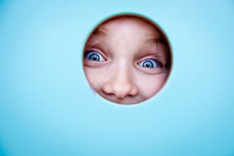 A child looks through a hole in the door